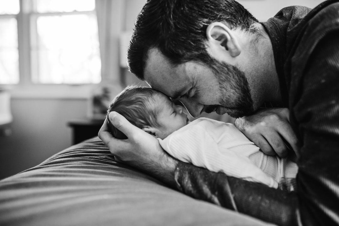 Father gently kissing sleeping newborn baby in black and white photo.