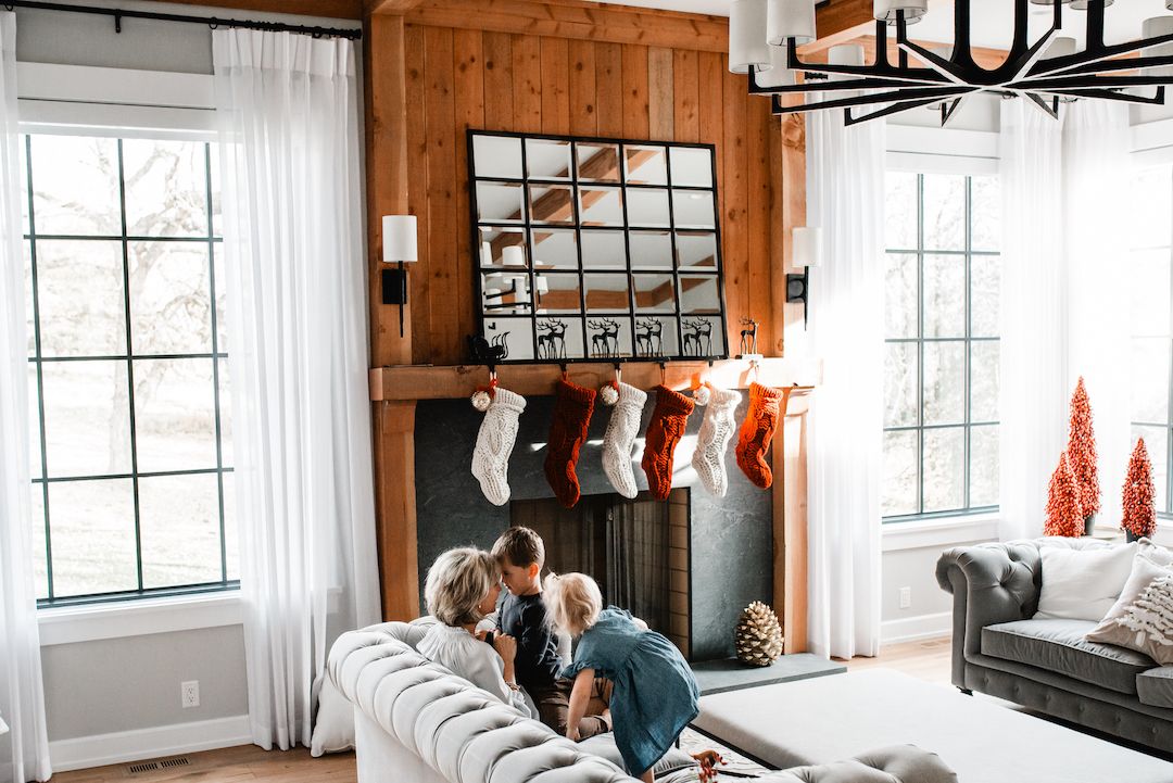 Family cuddling on a tufted sofa near a fireplace decorated with Christmas stockings.