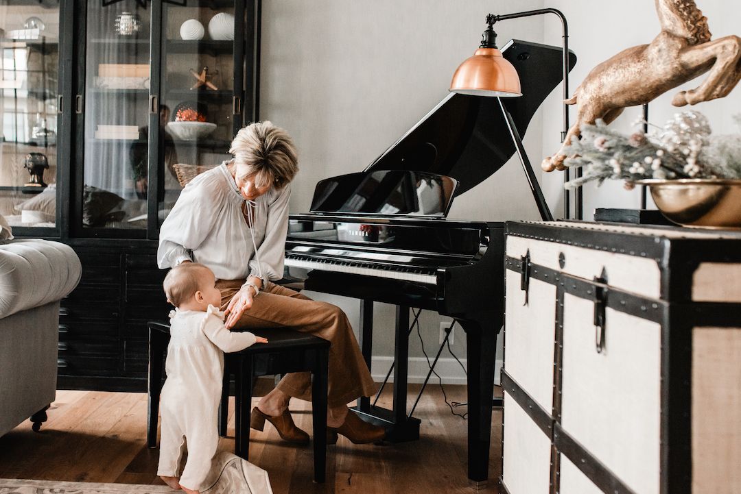 A grandmother teaches her grandchild to play a black grand piano in an elegant home.