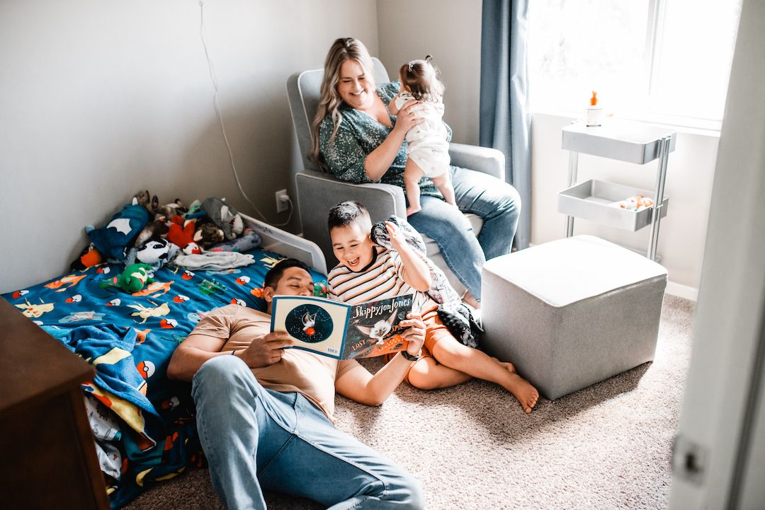 Family relaxing in a childs bedroom with parents reading and holding children.