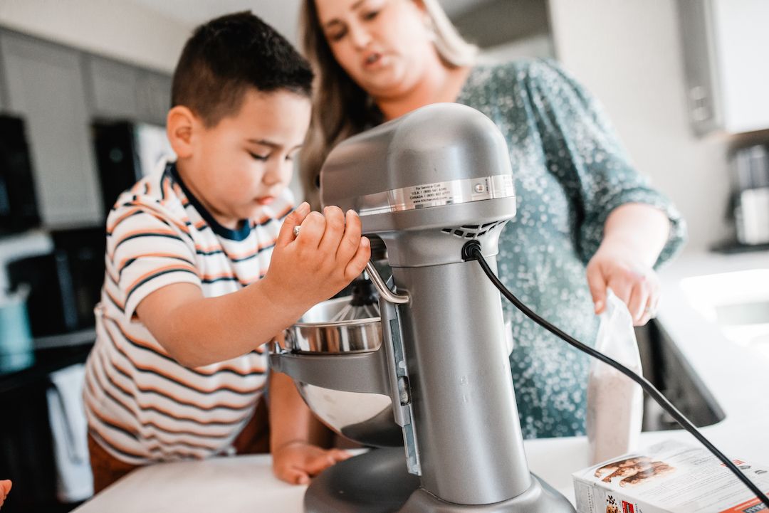 Young boy and mother using a KitchenAid stand mixer together in kitchen.