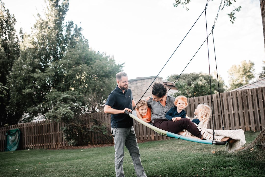 Family with children enjoying a large backyard rope swing together outdoors.