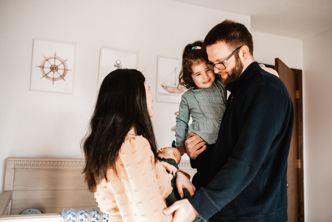 Happy family moment with parents and toddler smiling in a bright bedroom nursery setting.