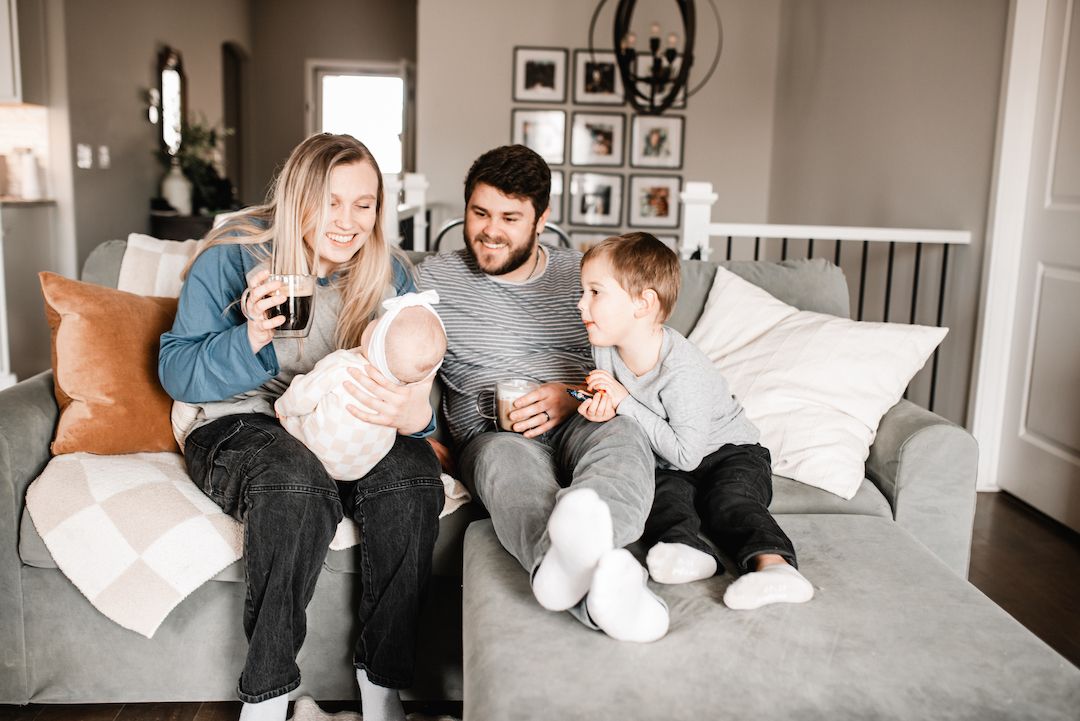 Happy family of four sitting together on a gray couch in a modern living room, sharing a joyful moment.