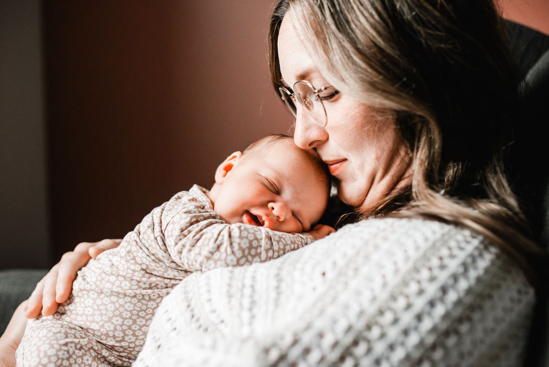 A mother tenderly holds her sleeping newborn baby wrapped in a floral swaddle, sharing a peaceful moment.