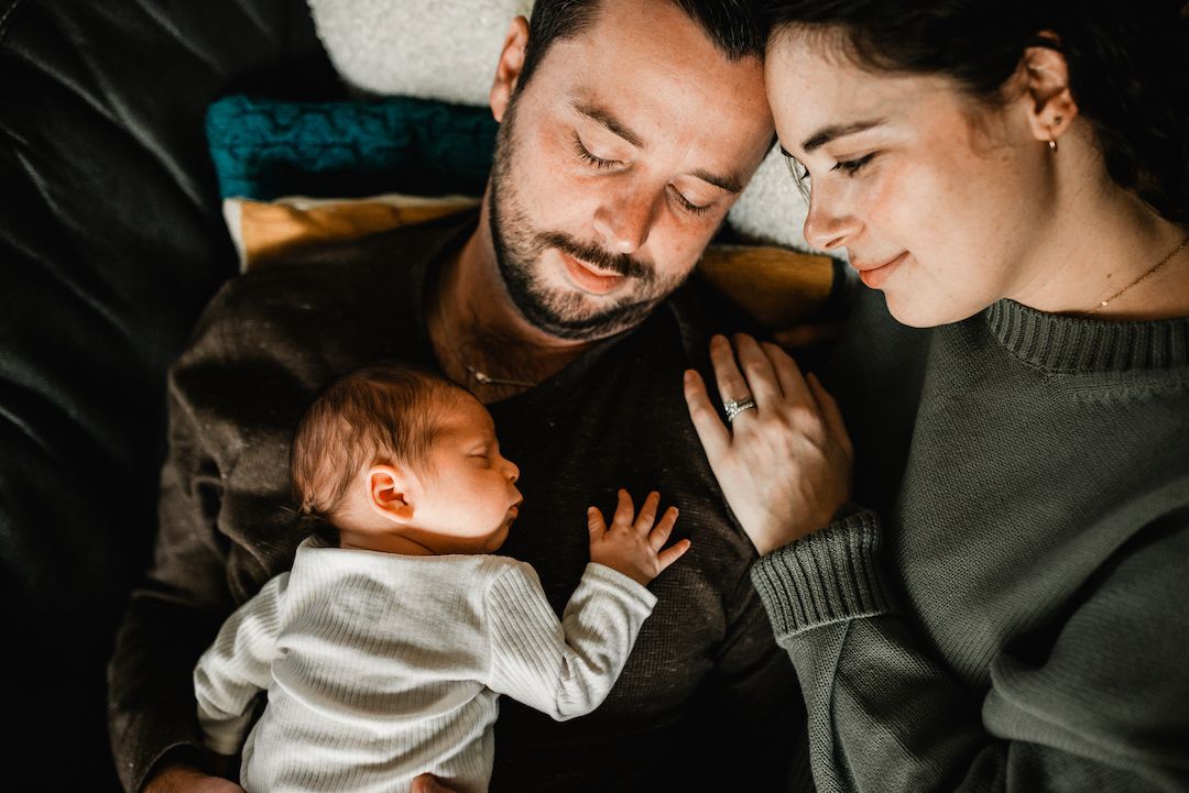 New parents gazing lovingly at sleeping newborn baby in tender moment.
