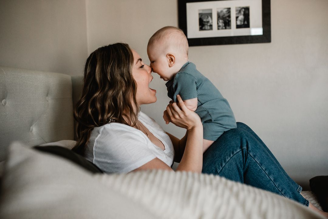 Loving mother holding baby close for a kiss while lying on bed.