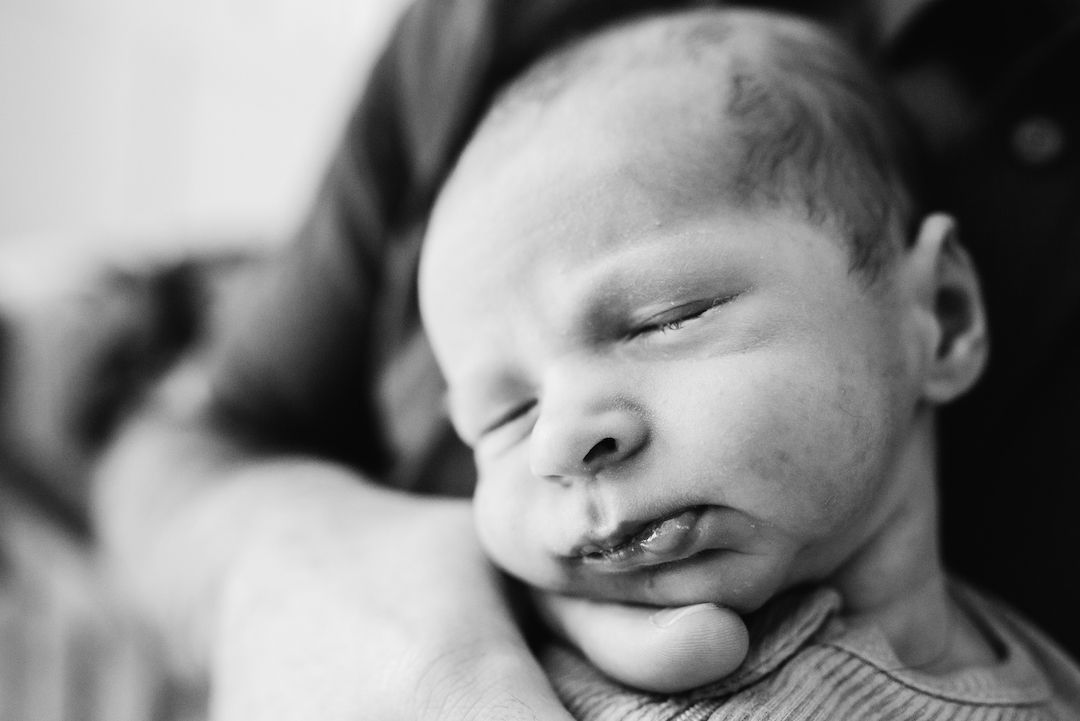 Black and white close-up of a peaceful sleeping newborn baby cradled in adult arms.