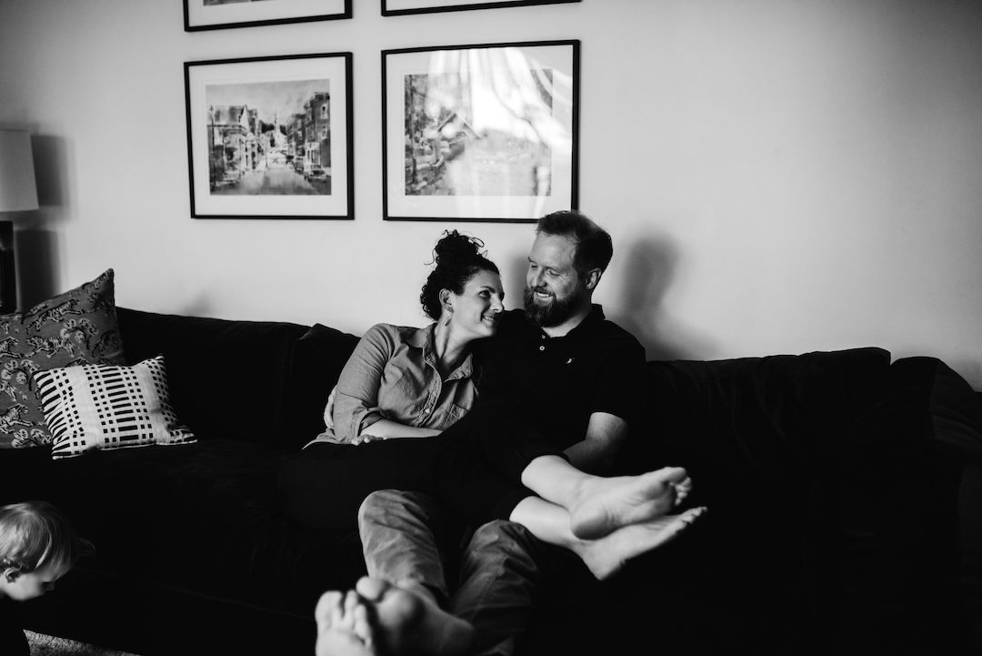 Couple sharing a tender moment on a black couch in a cozy living room, black and white photo.