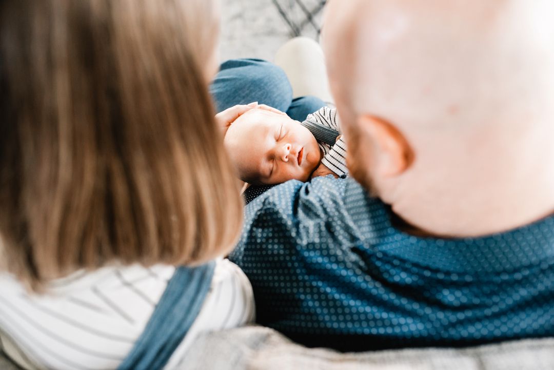Two parents gazing lovingly at their sleeping newborn baby wrapped in a blue blanket.