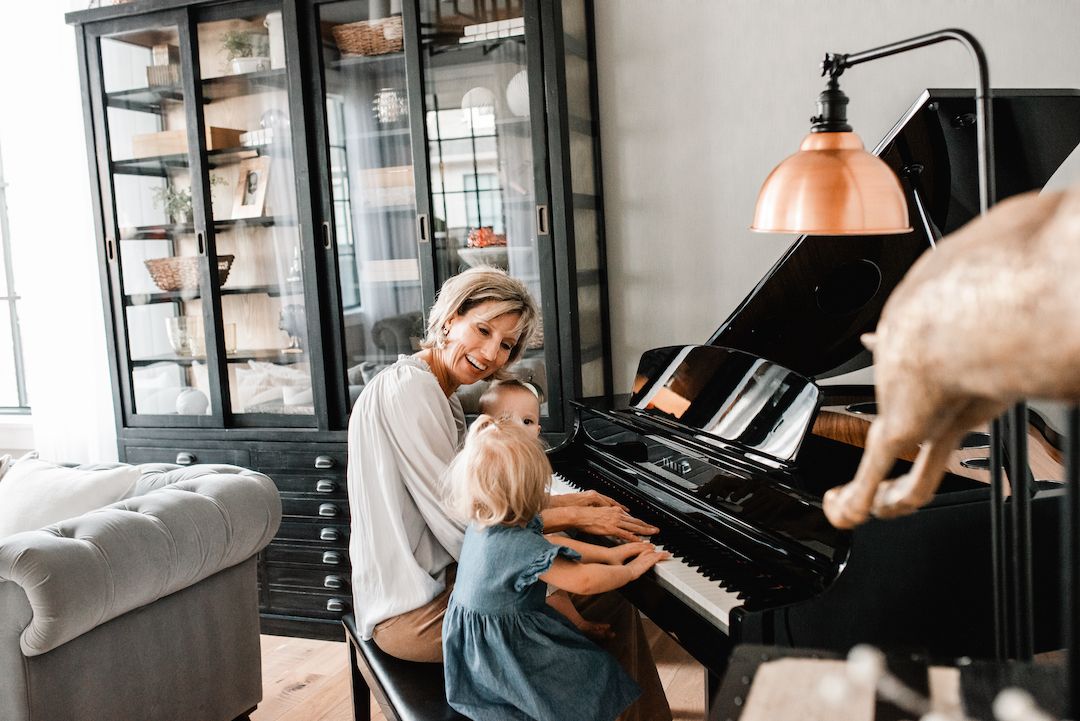 Woman and young girl playing a black grand piano together in a stylish modern living room.