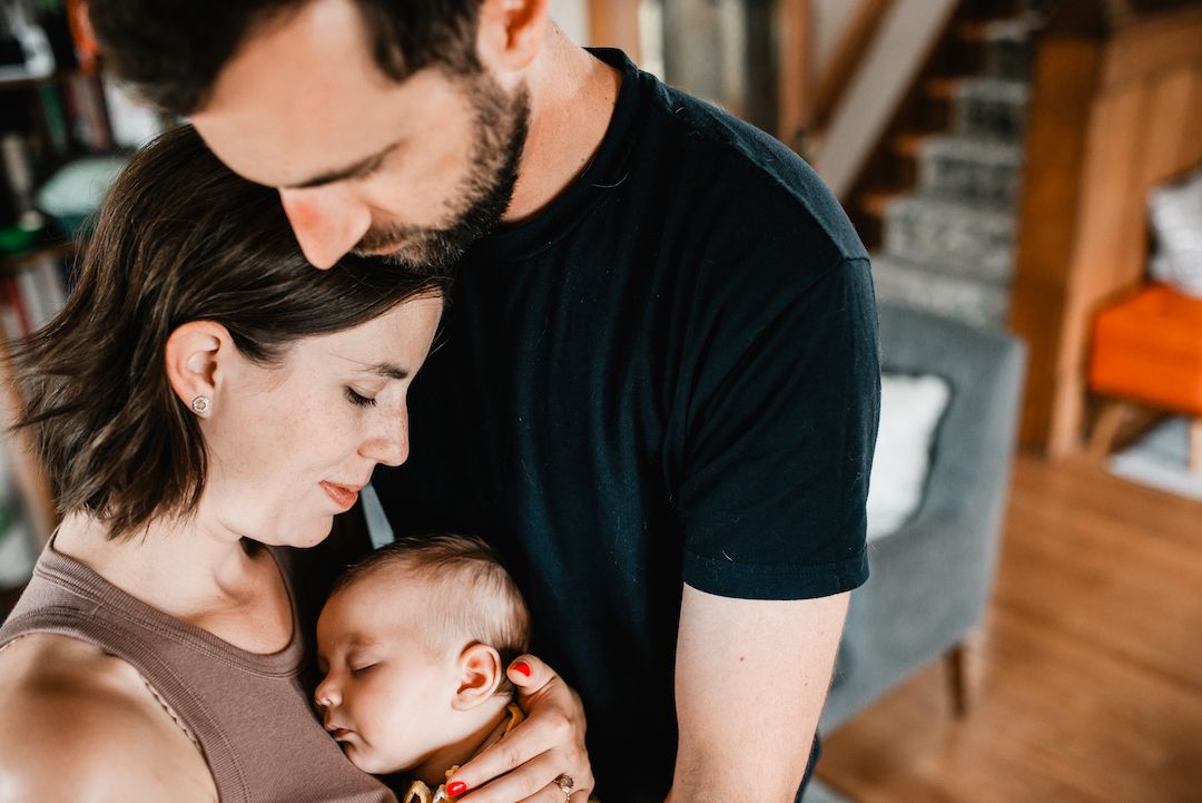 A couple tenderly holds their sleeping newborn baby together in a warm, intimate home setting.