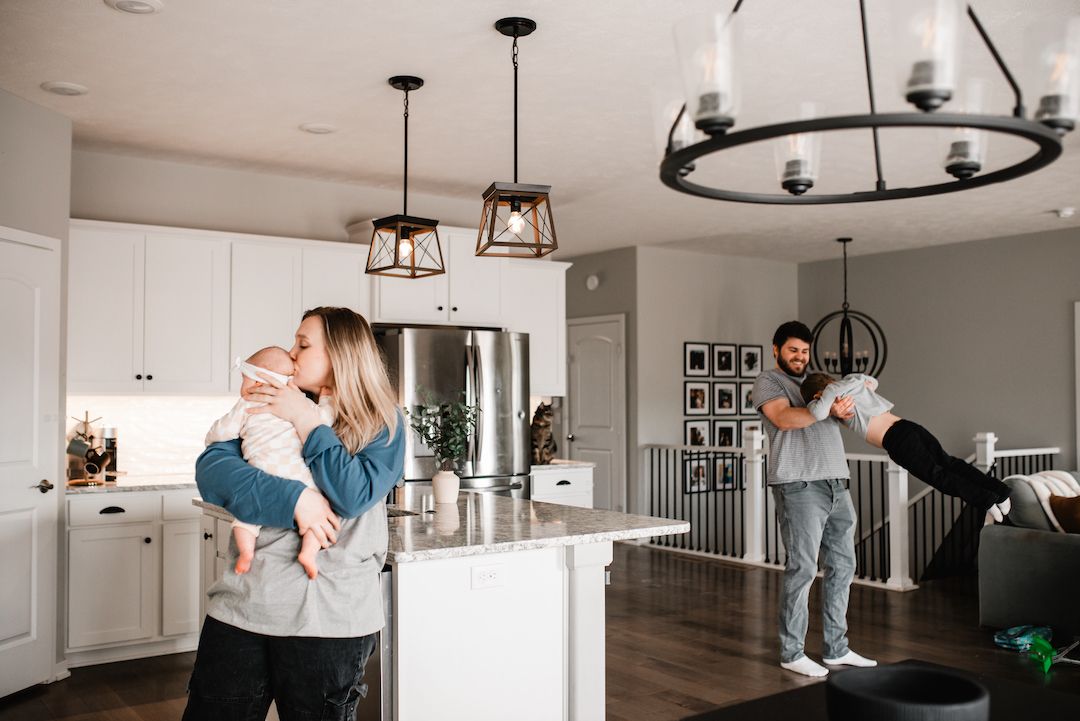 Happy family with two children playing in a modern white kitchen with pendant lights overhead.