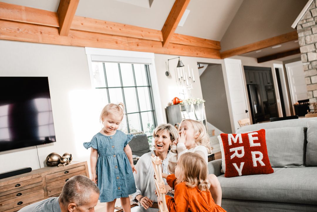 Family laughing and playing together in a cozy living room decorated with holiday pillows.