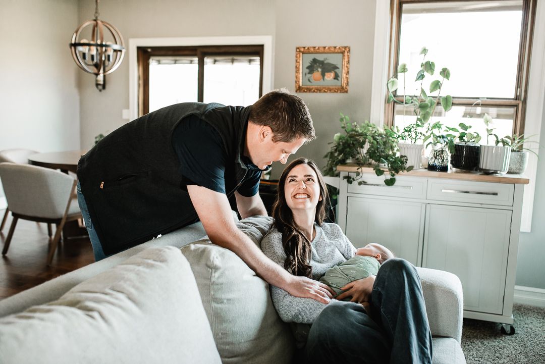 A couple shares a joyful moment on a cozy living room couch, with lush plants and warm home decor in the background.