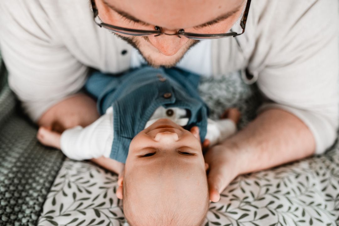 Loving father kissing his newborn baby on a patterned surface from above.