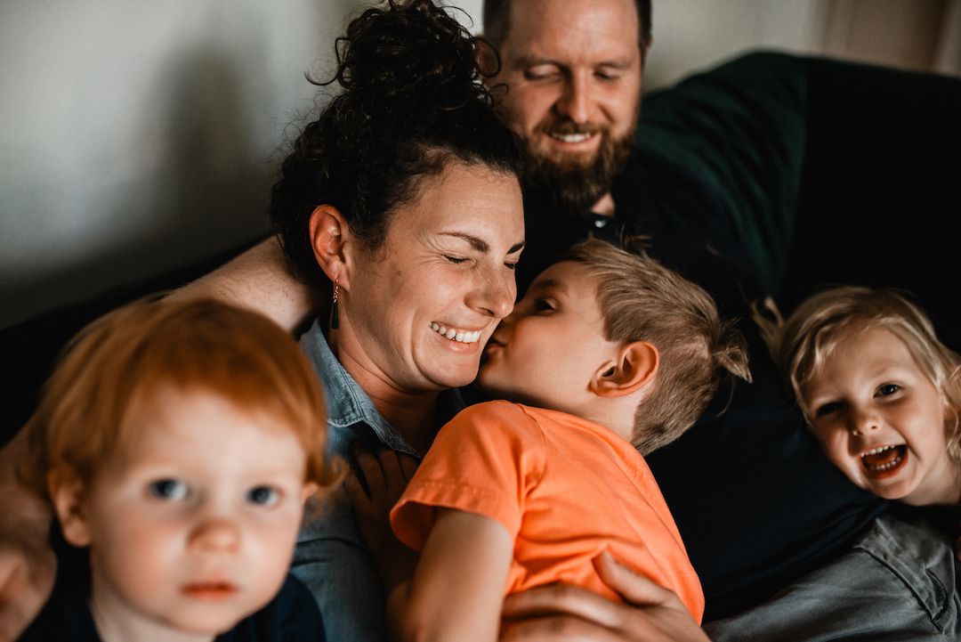 Joyful mother being hugged and kissed by her children while sitting on a couch.