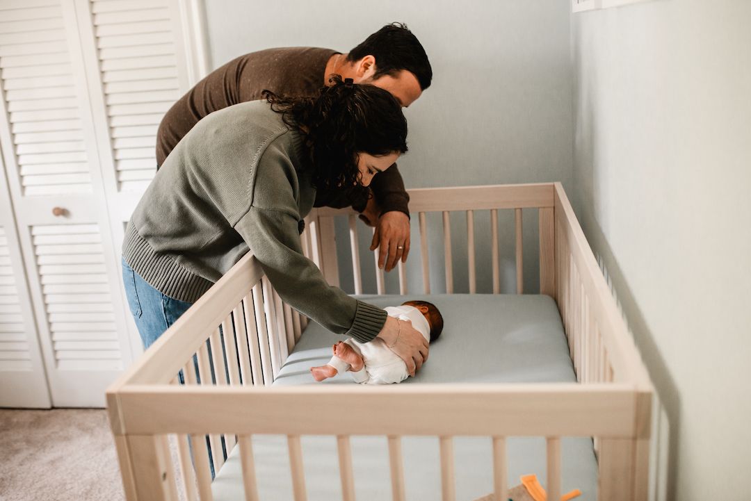 Parent gently placing a newborn baby in a wooden crib in a nursery room.