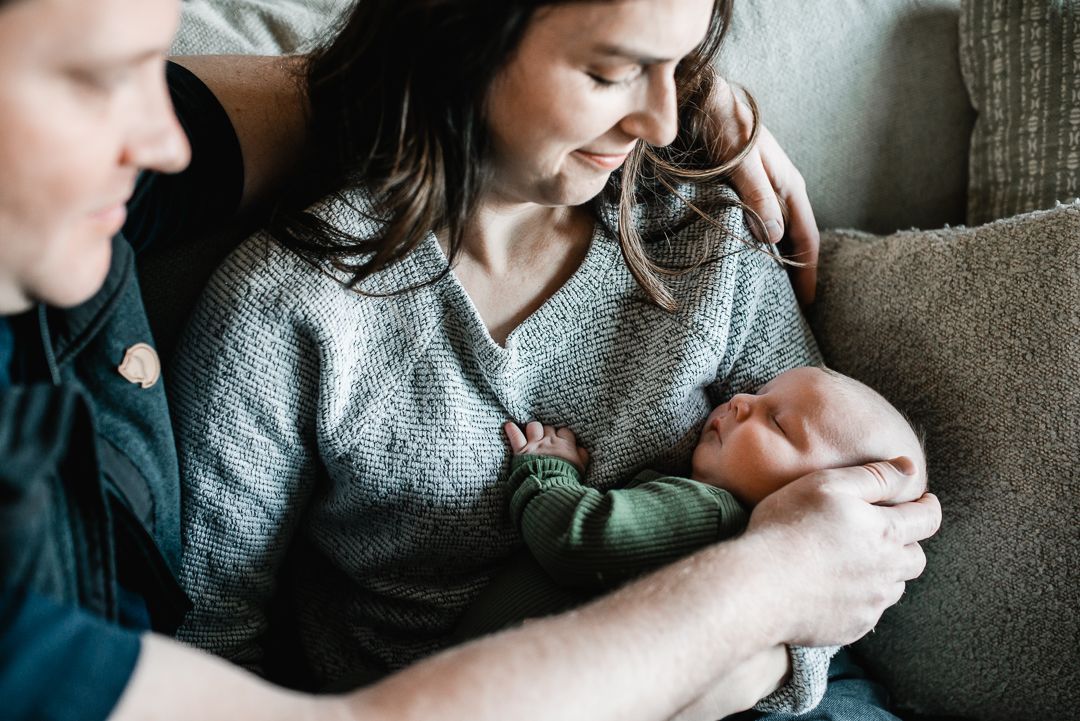 Parents sitting on a couch lovingly gazing at their newborn baby, capturing a tender family moment.