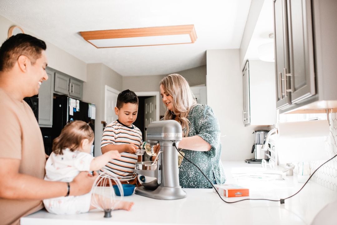 Family with two kids baking together using stand mixer in kitchen.