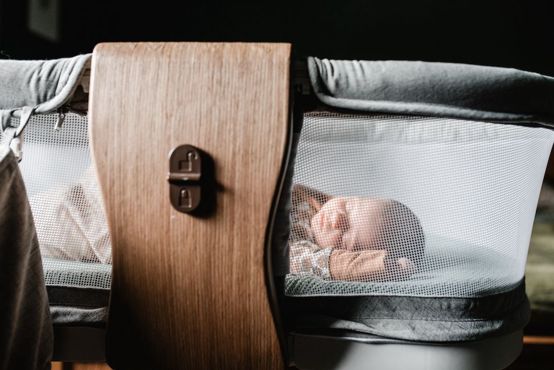 Newborn baby sleeping peacefully inside a modern bassinet with wooden panel detail.