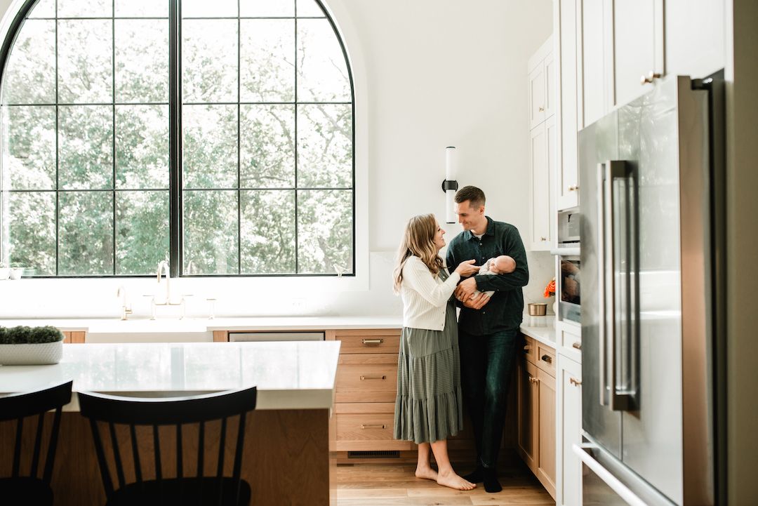 Couple sharing a tender moment in a modern kitchen with arched window, natural light, and warm wood cabinetry.