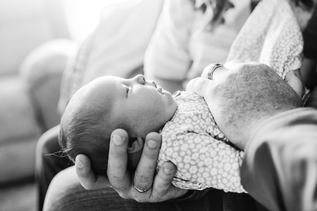 Black and white photo of a newborn baby cradled in an adult's hands while being held close.