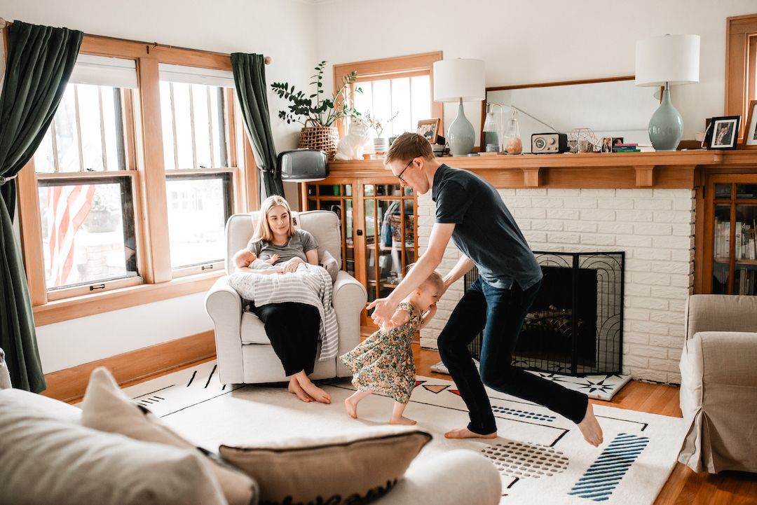 Family enjoying a playful moment in a cozy living room with a fireplace, dad swinging child while mom relaxes.