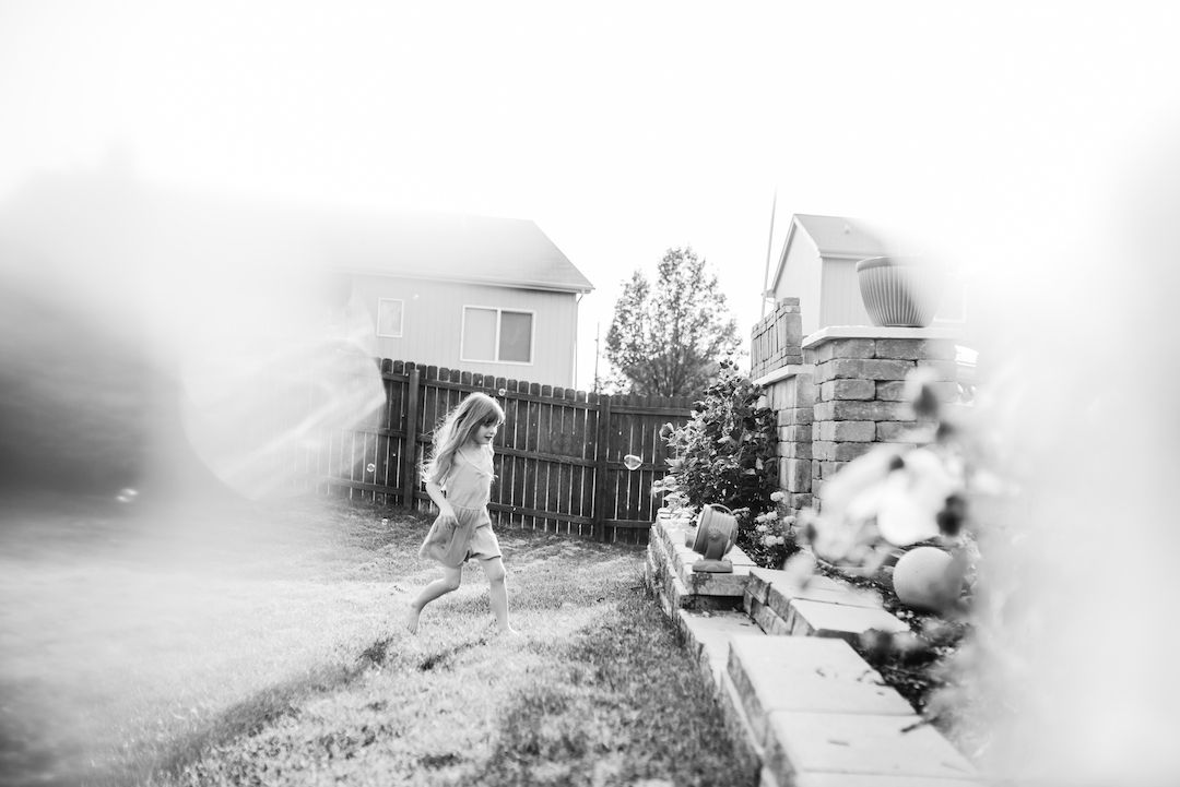 Black and white photo of a child running through a backyard in bright sunlight.