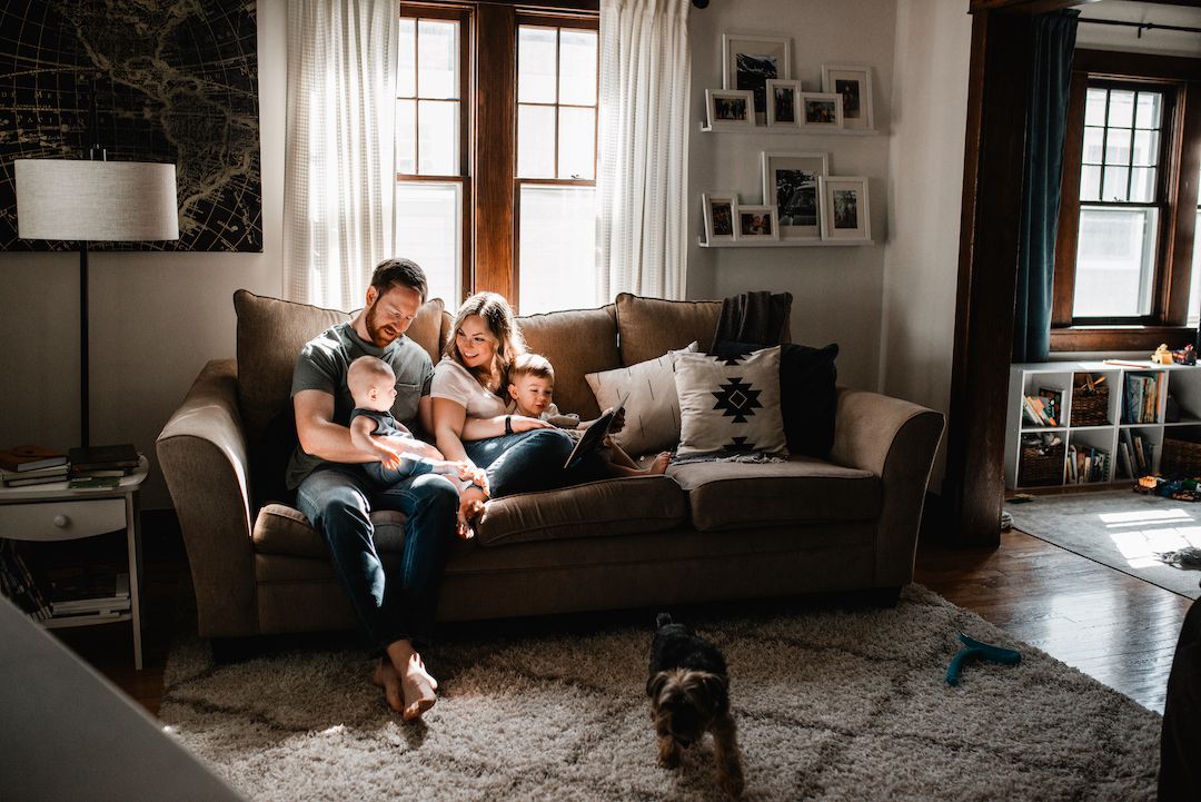 Family of four relaxing on a cozy couch reading together in a warm living room.