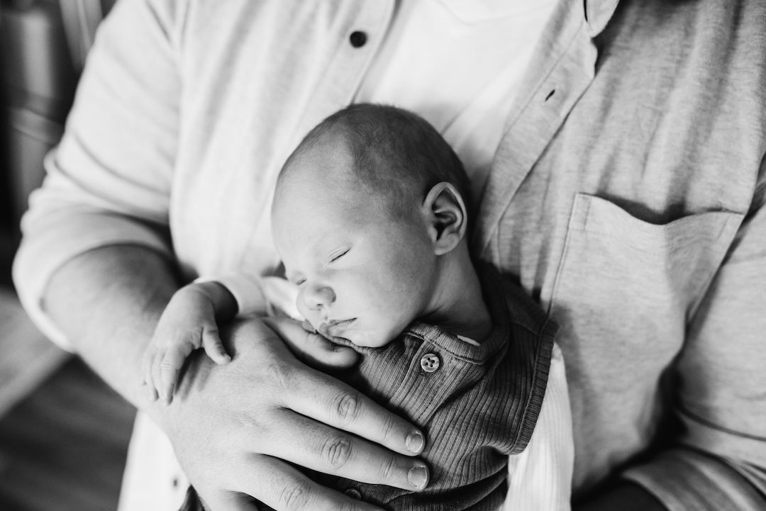 Black and white photo of a newborn baby sleeping peacefully in the gentle hands of a parent.