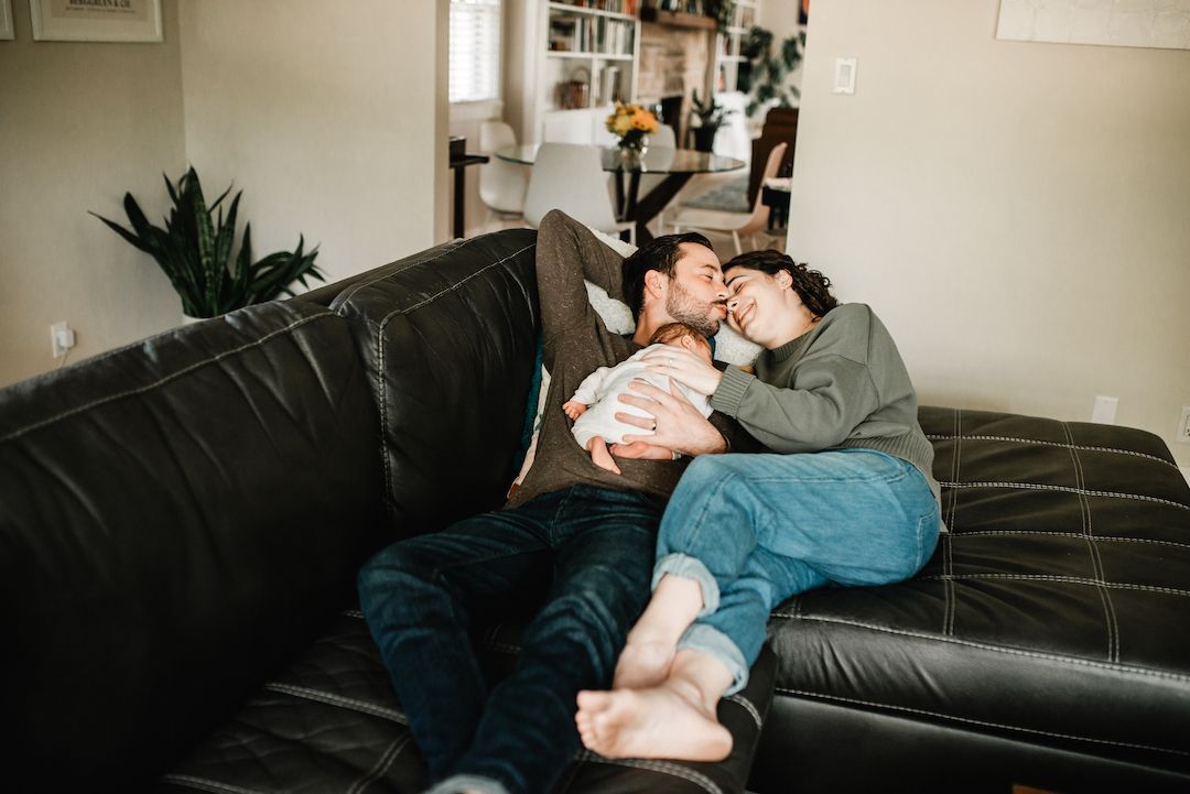 Couple relaxing on a black leather sofa, cuddling together in a cozy living room setting.
