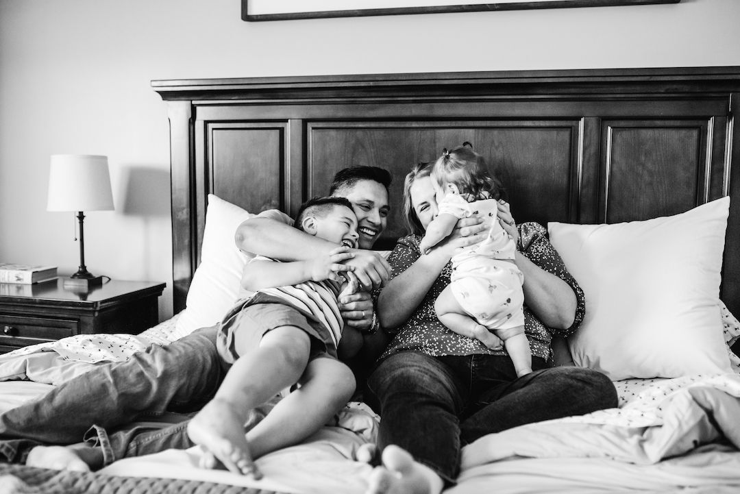 Black and white photo of parents cuddling with their young child on a bed.