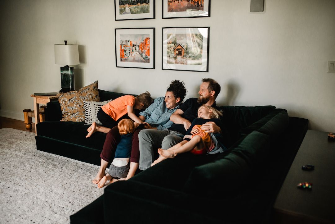A happy family relaxes together on a dark green sofa in a cozy living room.