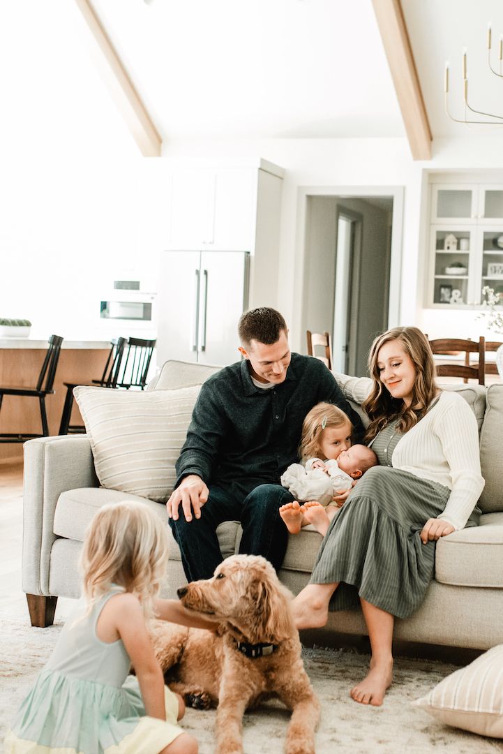 Happy family with two children and a golden doodle dog relaxing together on a couch in a bright home.