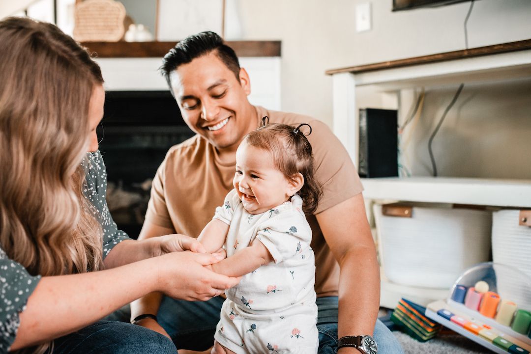 Smiling parents playing with their happy laughing baby in a bright home setting.