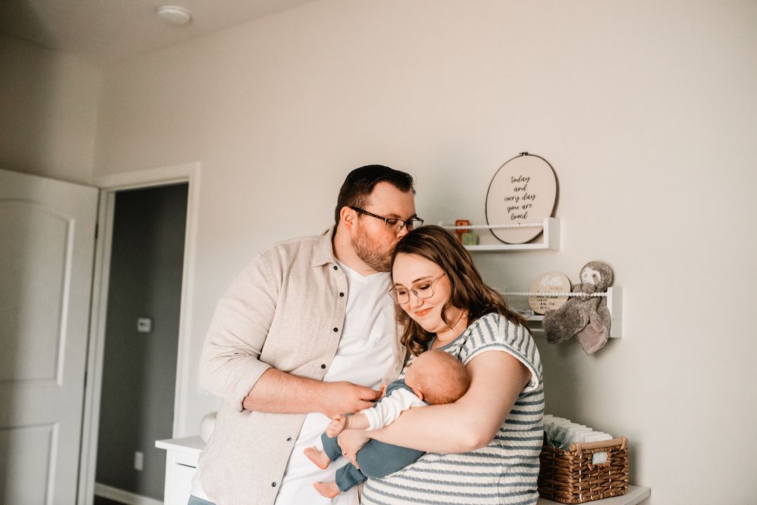 New parents tenderly holding their newborn baby together in a cozy nursery room.