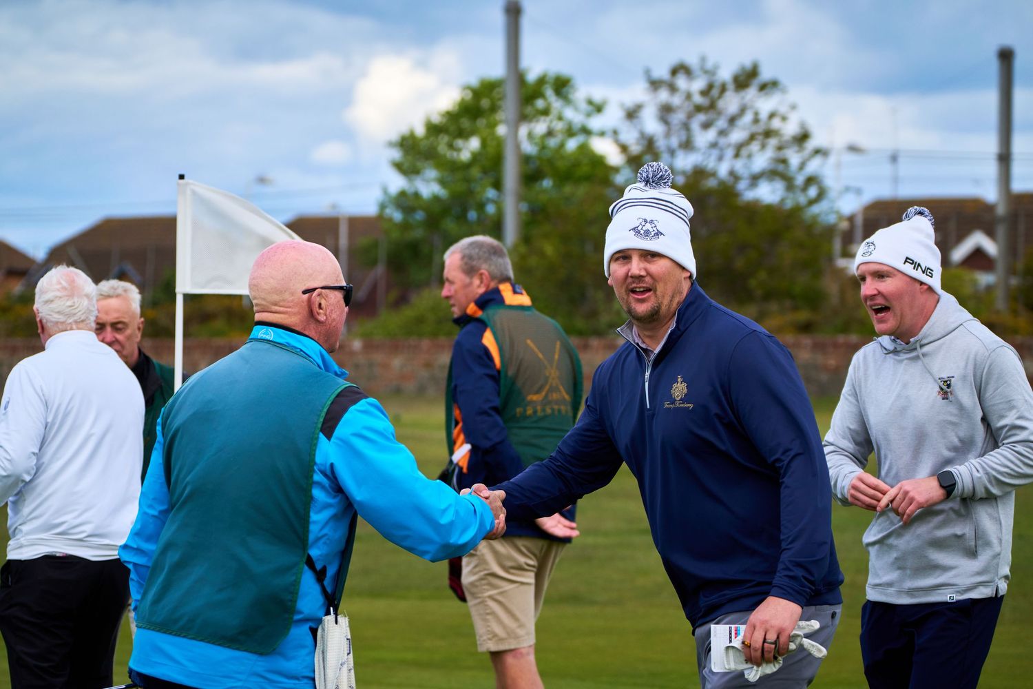 Golfers exchanging handshakes and smiling on a golf course during a friendly competition.