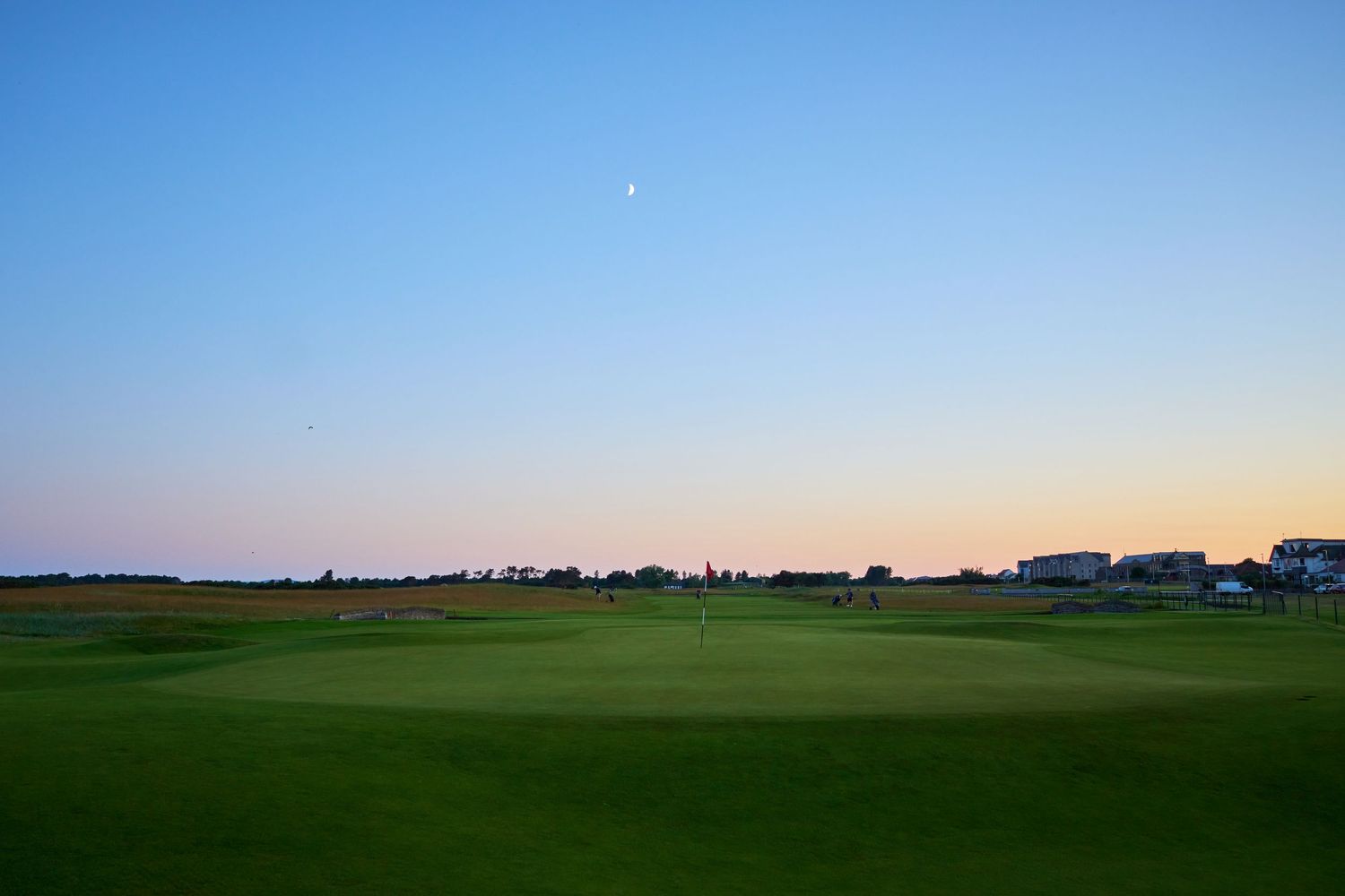 Serene twilight view of a links golf course green with a flagstick under a pastel evening sky.