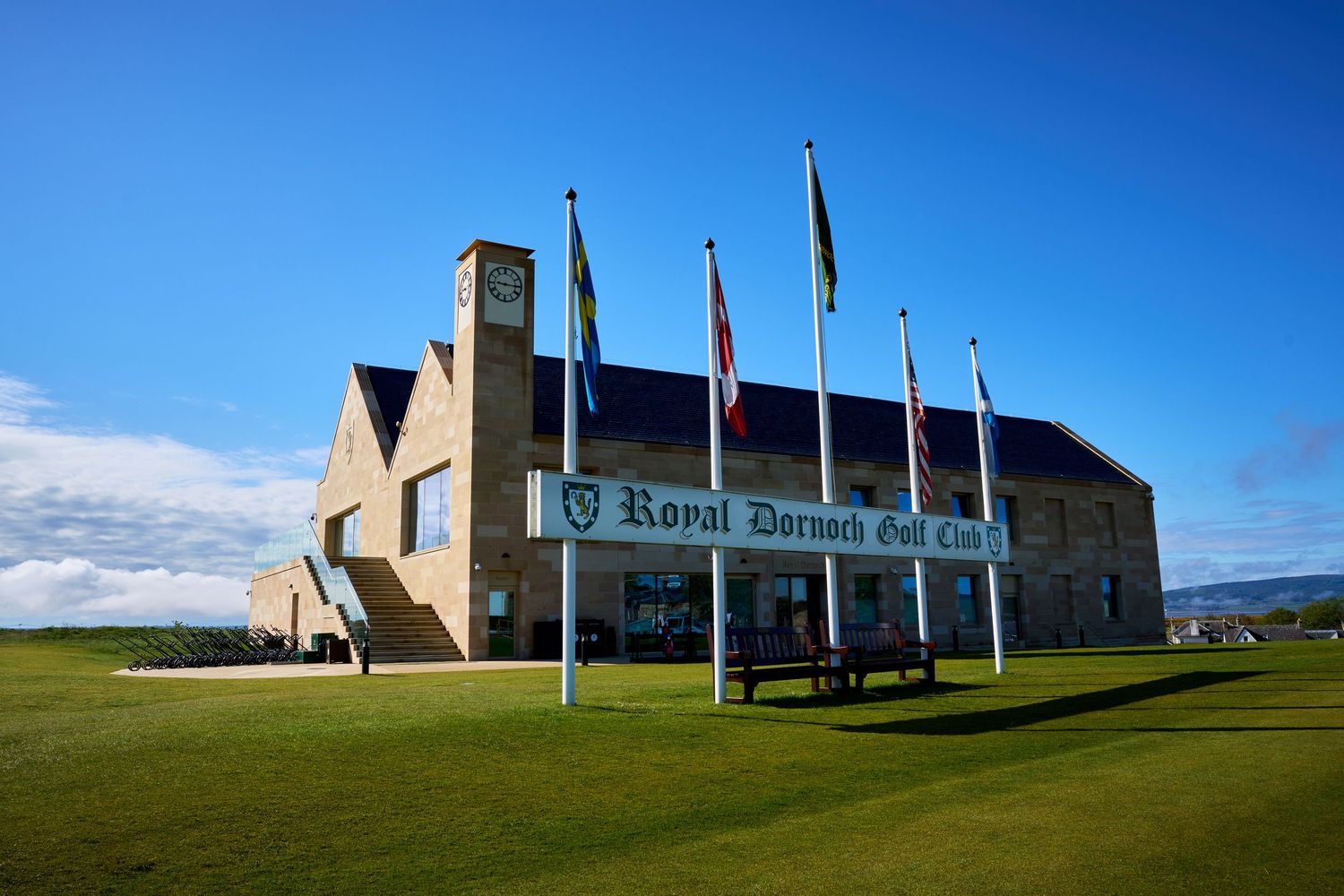 Royal Dornoch Golf Club clubhouse with flags under a bright blue sky in Scotland.