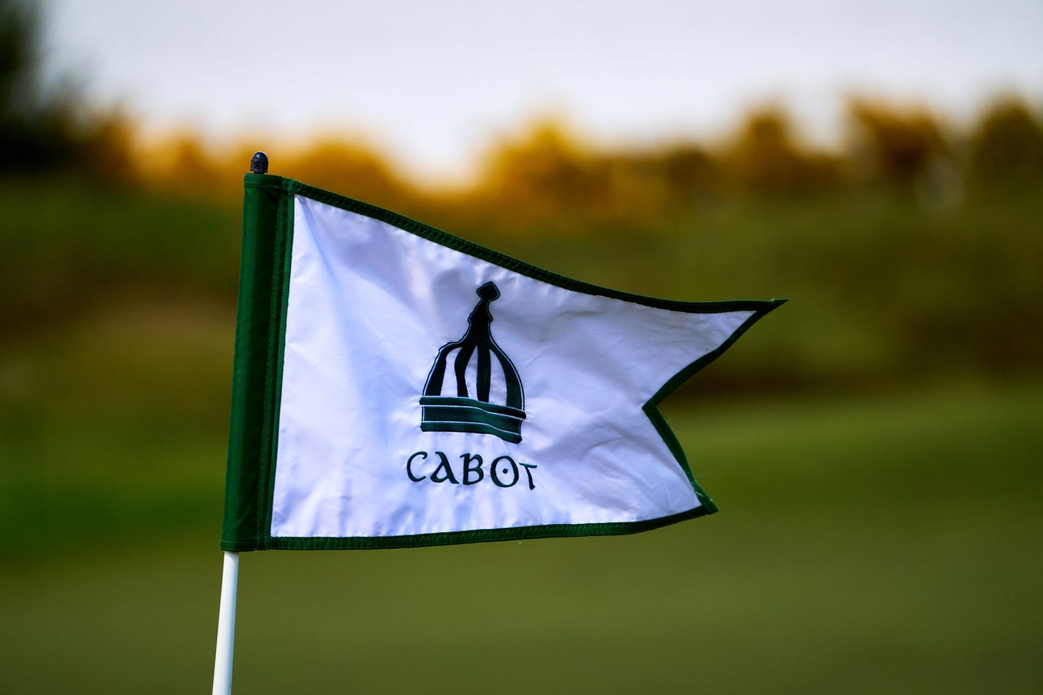 Cabot golf course flag on a white pennant with green trim, featuring the iconic crown logo on a putting green.