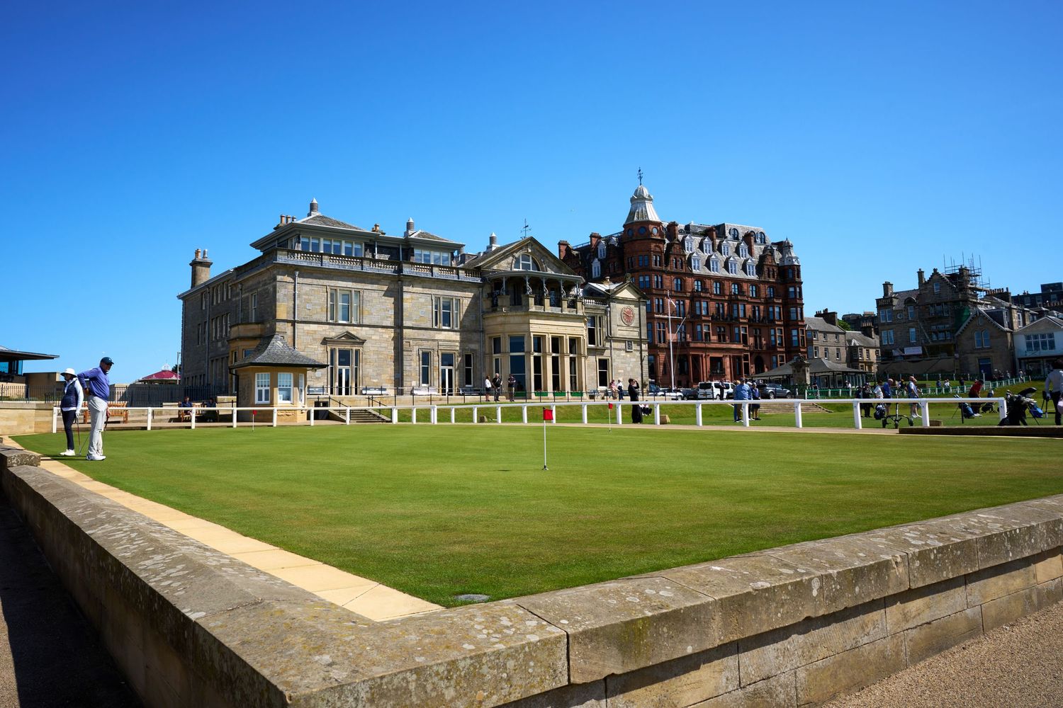 Historic St Andrews golf clubhouse with manicured green lawn under clear blue sky in Scotland.
