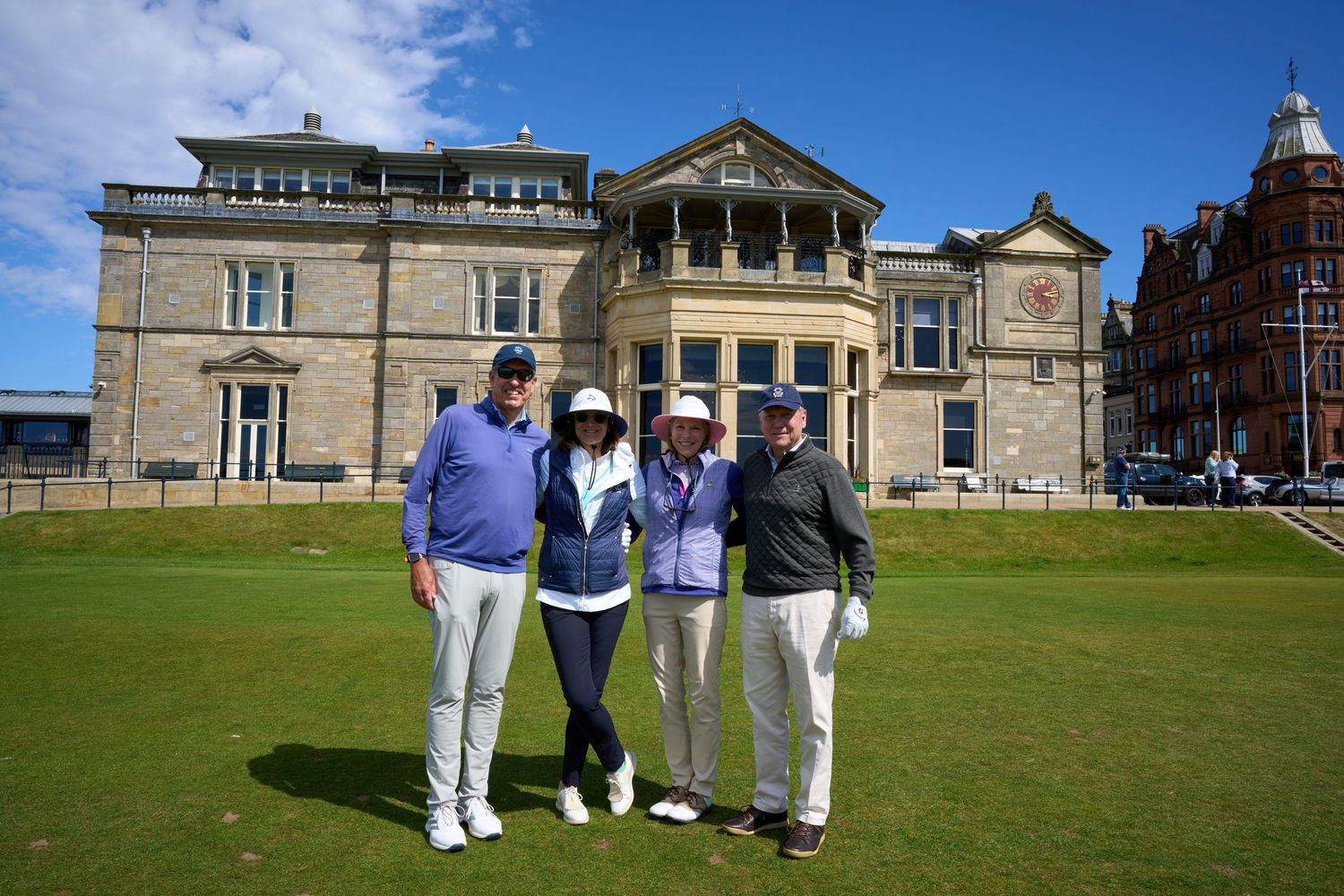Four golfers pose together on the 18th green at St Andrews Old Course with the iconic clubhouse behind them.