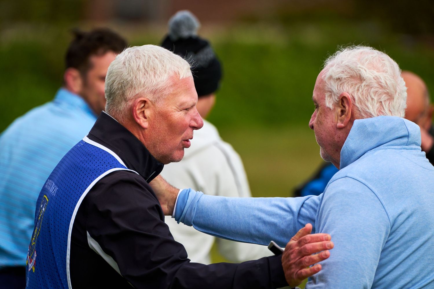 Two older men in golf attire having an animated conversation on a golf course.