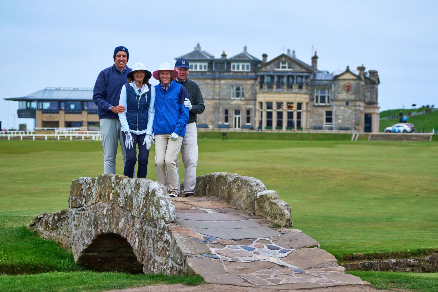 Three golfers posing on the iconic Swilcan Bridge at St Andrews Old Course in Scotland.