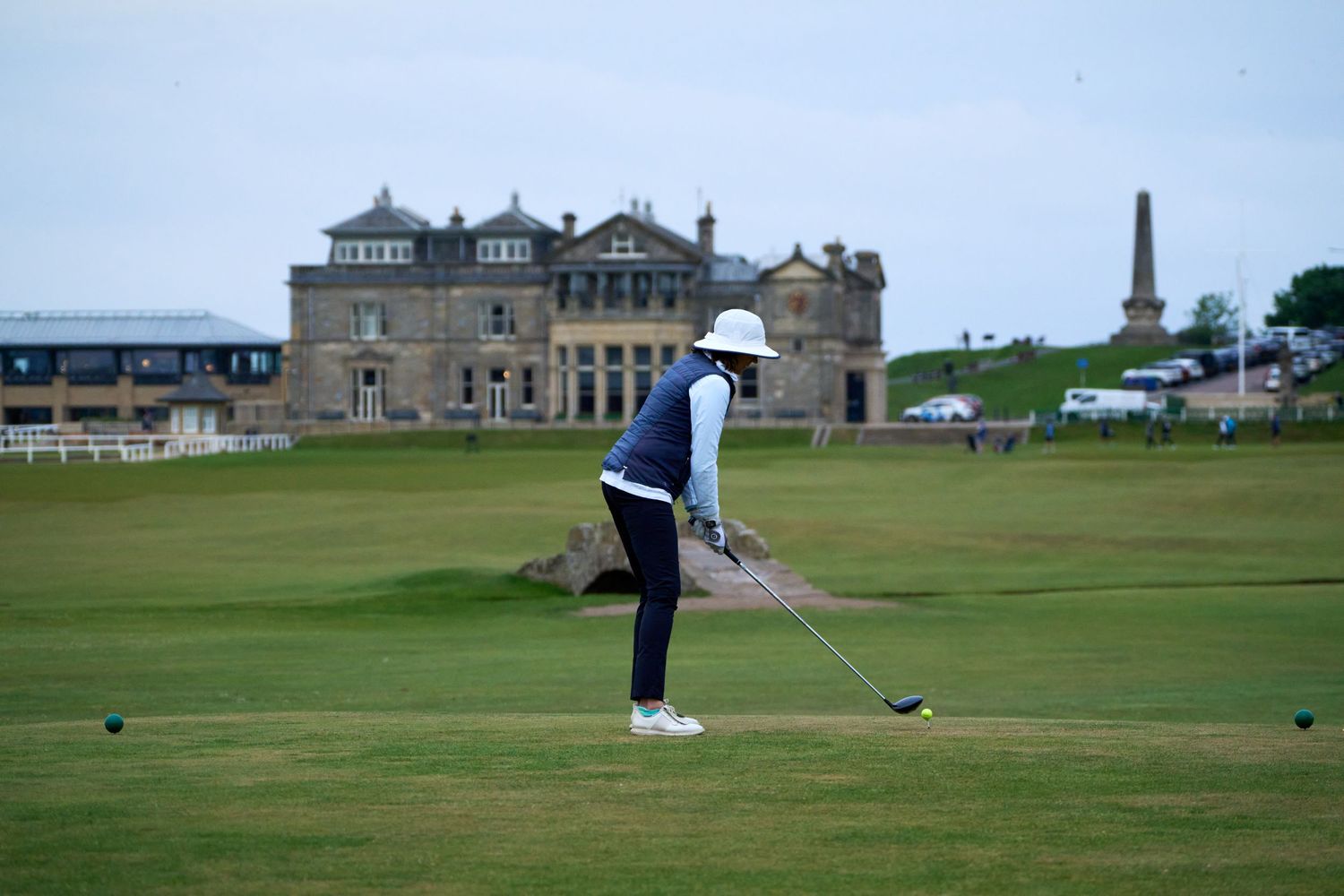 Golfer teeing off at St Andrews Old Course with the iconic Royal and Ancient clubhouse in the background.