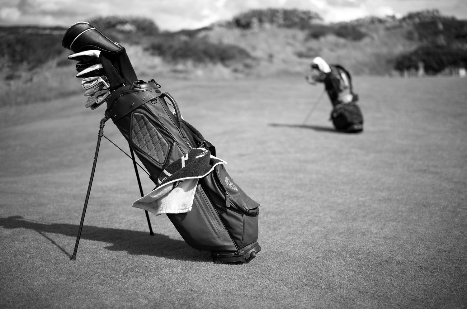 Black and white photo of two golf bags standing on a links golf course fairway.