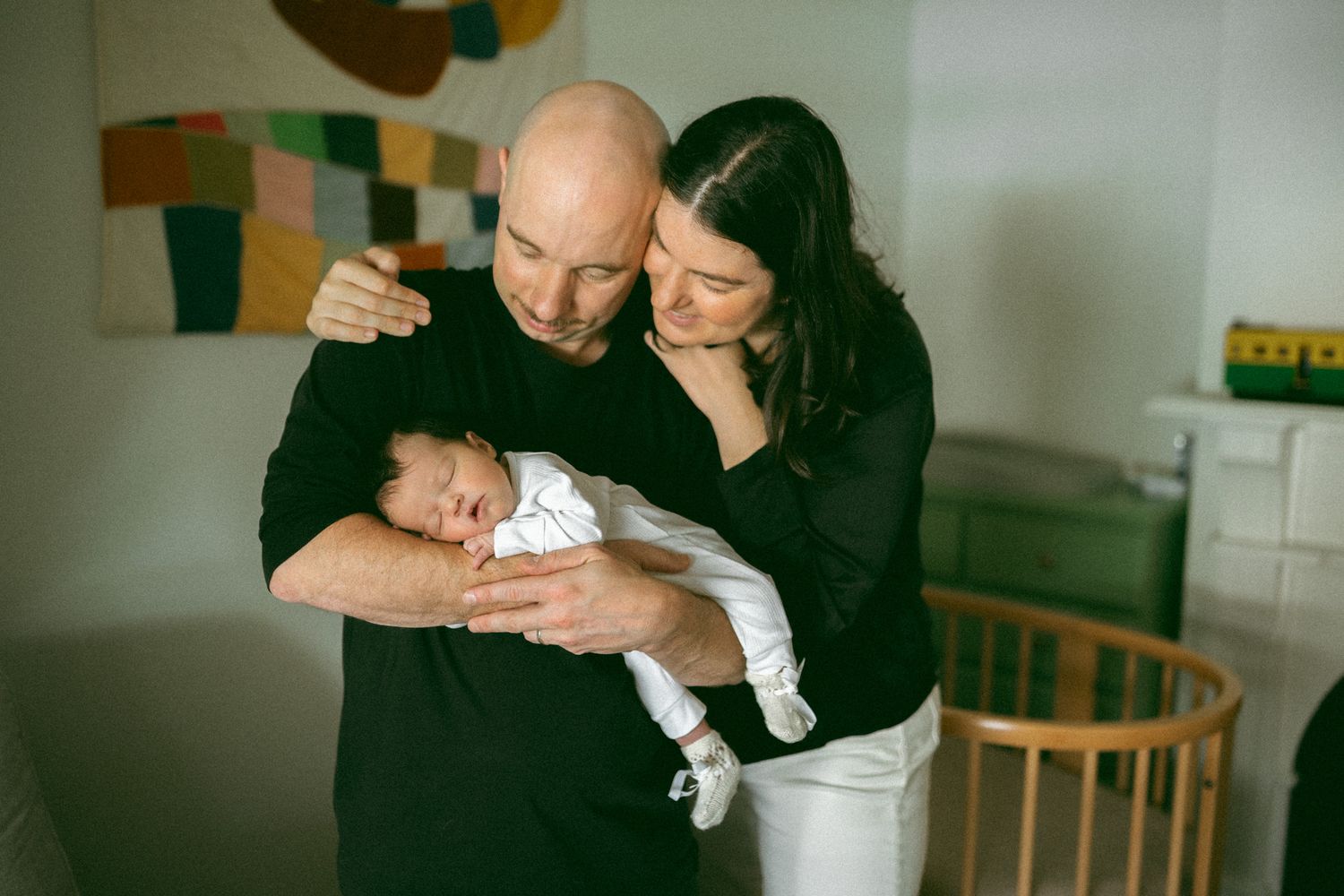 New parents tenderly hold their sleeping newborn baby in a cozy nursery room.