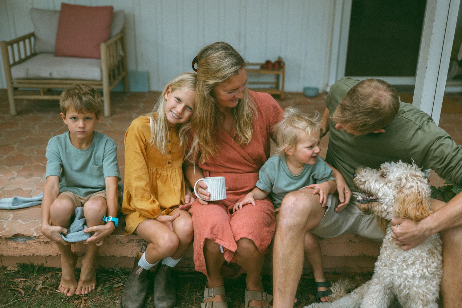 Happy family with two children and a dog sitting together on a porch steps, enjoying a relaxed outdoor moment.