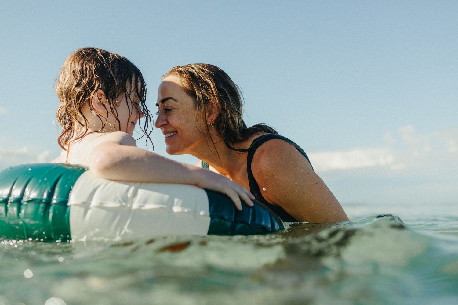 Woman and child playing in ocean waves, child floating on inflatable ring while smiling woman holds them close.